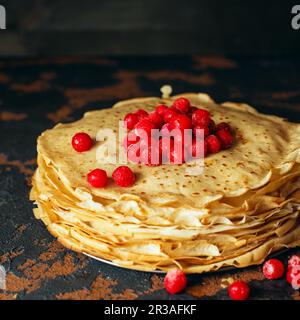 Russische Pfannkuchen mit Beeren vor dunklem Hintergrund. Pfannkuchenwoche - das alte slawische Fest Stockfoto