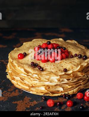 Russische Pfannkuchen mit Beeren vor dunklem Hintergrund. Pfannkuchenwoche - das alte slawische Fest Stockfoto