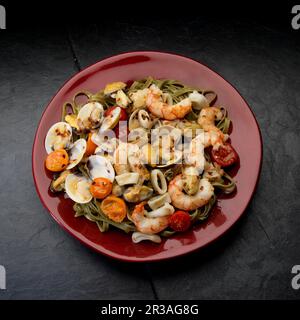 Mediterrane Meeresfrüchte, Weißwein, Garnelen, Muscheln, Muscheln, Calamari, Tomaten auf schwarzem Teller Stockfoto