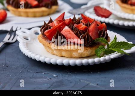 Minitarte mit Erdbeermarmelade, serviert mit frischen Erdbeeren und Schokoladenganache Stockfoto