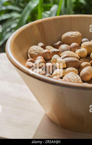 Verschiedene Nüsse in einer großen Holzschüssel auf einem blattgrünen Hintergrund Stockfoto