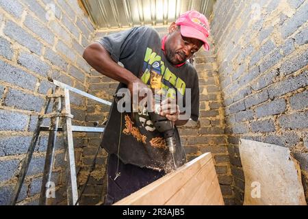 Afrikanischer Zimmermann arbeitet an einem Gemeindeverbandprogramm, um ein kleines, erschwingliches Haus in einer lokalen Gemeinde zu bauen Stockfoto