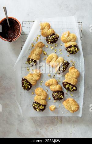 Butterkekse in dunkle Schokolade getaucht und mit Pistaziennüssen auf einem Kühlregal bestreut Stockfoto