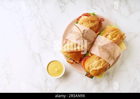 Frische große Baguette-Sandwiches mit Speck, Käse, Senf, Salat und Gemüse Stockfoto