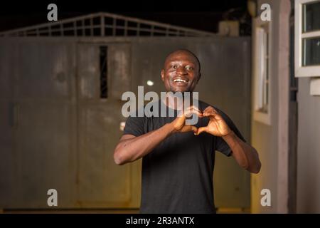 Ein gut aussehender afrikaner, der beide Hände legt und das Herzsymbol auf seine Brust legt. Ich zeige eine erleichterte Geste Stockfoto