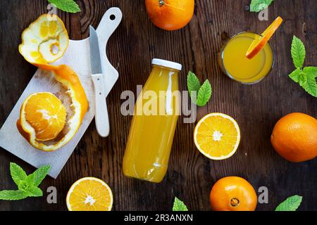 Orangensaft in einem Glas und Flasche mit frischen Orangen und Minzblättern Stockfoto