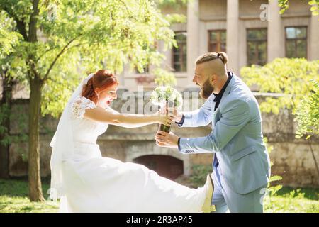 Gerade verheiratetes, liebevolles Hipsterpaar in Hochzeitskleid und Anzug im Park. Fröhlicher Braut-Bräutigam-Spaziergang Stockfoto