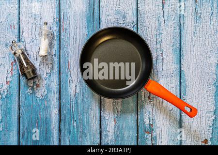 Eine leere Pfanne zusammen mit einer Salz- und Pfeffermühle auf einem blauen Tisch Stockfoto