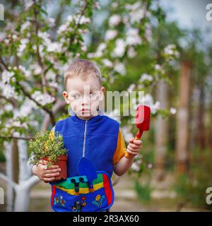 Hübscher kleiner blonder Junge, der Blumen im Garten pflanzt und gärtnerisch arbeitet Oder Bauernhof im Frühling Tag Stockfoto