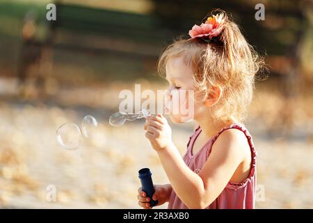 Ein kleines Mädchen bläst Seifenblasen im Herbstpark Stockfoto