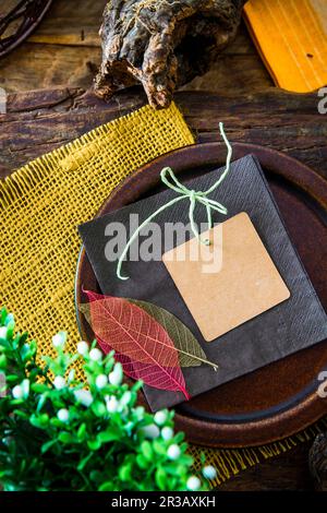 Platzieren Sie das Ambiente mit einer Karte und Blattdekorationen auf einem rustikalen Holztisch Stockfoto