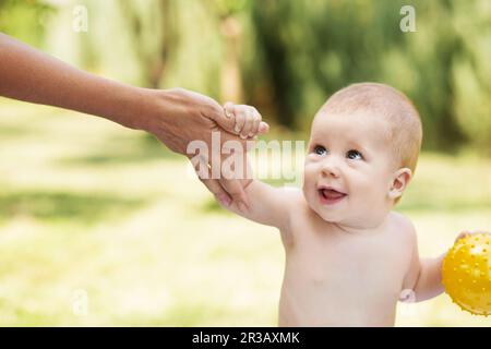 Porträt eines schönen Babys, das die Hand der Mutter entgegenhält Grüne Natur Hintergrund im Freien Stockfoto