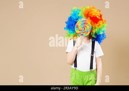 Glücklicher Clownjunge in einer großen, bunten Perücke. Lasst uns feiern! Lustiger kleiner Clown. 1 April Fool's Day Konzept. Por Stockfoto