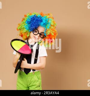 Unverschämte Kinder. Porträt eines glücklichen Clownjungen mit einer großen neonfarbenen Perücke. Ein Junge mit Clown Perücke A. Stockfoto