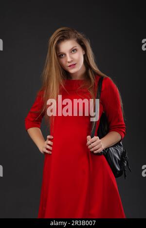 Porträt eines Mädchens in einem roten Kleid mit einem schwarzen Lederrucksack auf der Schulter. Stockfoto