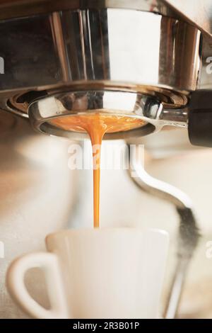 Ein Shot Espresso, der aus einem Portafilter in eine weiße Espressotasse extrahiert wird Stockfoto