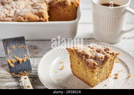 Ein Stück Krümelkuchen, serviert auf einem weißen Teller mit einer weißen Kaffeetasse gefüllt mit Kaffee Stockfoto