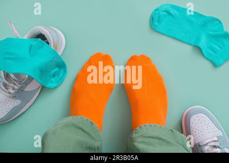 Die Füße eines Mannes in orangefarbenen Socken mit seinen Turnschuhen ziehen ab. Mintgrüner Hintergrund Stockfoto