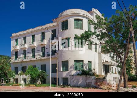 Ein flaches, verlassenes Hotel aus den 1930er Jahren mit einer verfallenen Fassade und grünen Holzfensterläden unter dem blauen Sommerhimmel. Stockfoto