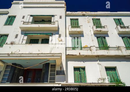 Ein flaches, verlassenes Hotel aus den 1930er Jahren mit einer verfallenen Fassade und grünen Holzfensterläden unter dem blauen Sommerhimmel. Stockfoto