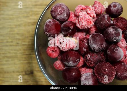 Ein Haufen aufgetauter roter Beeren in Einer Glasschale auf einer Holzfläche Stockfoto