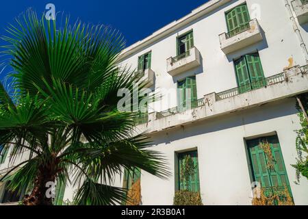 Ein flaches, verlassenes Hotel aus den 1930er Jahren mit einer verfallenen Fassade und grünen Holzfensterläden unter dem blauen Sommerhimmel. Stockfoto