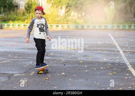 Kleiner Stadtjunge mit einem Penny Skateboard. Ein junger Junge, der auf einem Skateboard im Park reitet. City-Style. Stockfoto