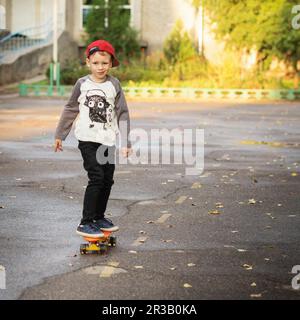 Kleiner Stadtjunge mit einem Penny Skateboard. Ein junger Junge, der auf einem Skateboard im Park reitet. City-Style. Stockfoto