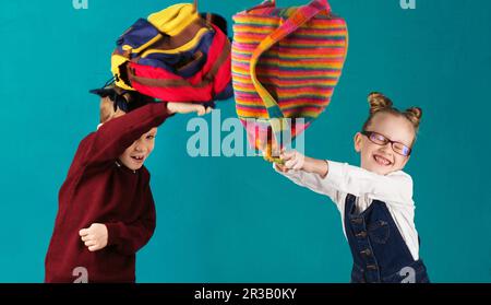 Lustige kleine Kinder, die einen großen Rucksack hüpfen und Spaß an der türkisfarbenen Wand haben. Schulkonzept. B Stockfoto