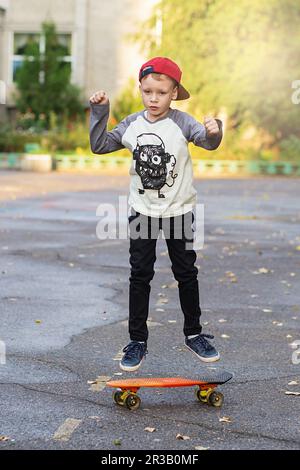 Kleiner Stadtjunge mit einem Penny Skateboard. Ein junger Junge, der auf einem Skateboard im Park reitet. City-Style. Stockfoto