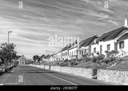 Elim, Südafrika - 21. September 2022: Eine Straßenszene mit historischen Häusern und der mährischen Kirche in Elim, in der Provinz Westkap. Schwarzweiß Stockfoto