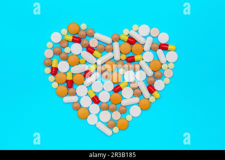 Medikamentenkapseln und -Pillen auf blauem Hintergrund. Mehrfarbige Pillen in Form des Herzens. Stockfoto