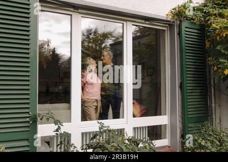 Seniorenpaar hinter dem Fenster ihres Hauses Stockfoto