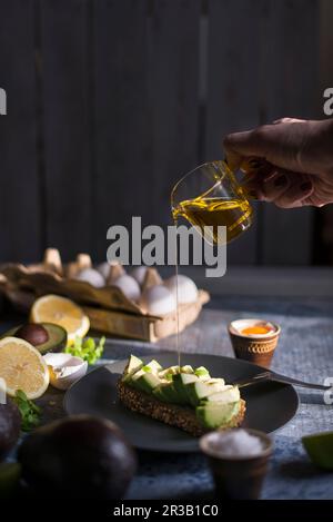 Olivenöl wird aus einer Glaskanne auf Avocadobrot gegossen Stockfoto