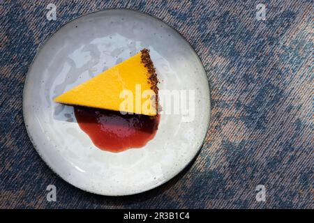 Ein Stück Mango-Torte mit Joghurt-Sahne, Keksbasis und Beerensauce Stockfoto