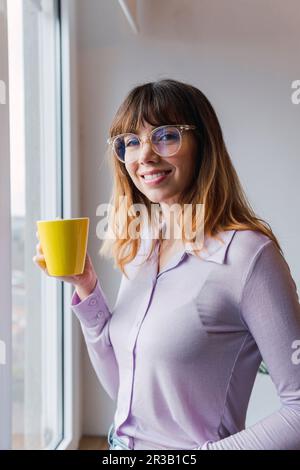 Glückliche Geschäftsfrau mit Kaffeetasse am Fenster Stockfoto