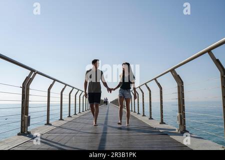 Ein junges Paar, das unter dem Himmel auf einer Brücke spaziert Stockfoto