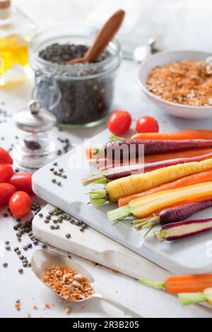 Regenbogenfarbene Möhren auf einem Schneidebrett mit Dukkah-Gewürzen Stockfoto