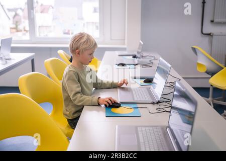 Ein blonder Junge, der in der Schule auf einem Stuhl sitzt Stockfoto