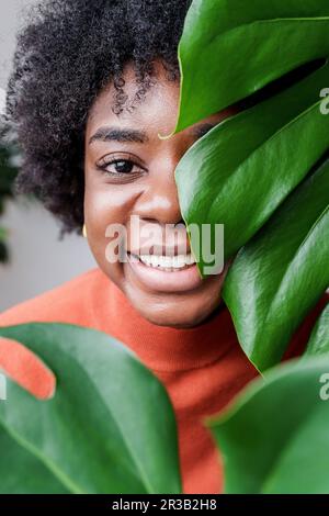 Eine lächelnde Frau, die hinter Monstera-Blättern steht Stockfoto