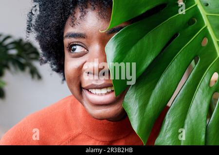 Lächelnde junge Frau mit Monsterabblättern Stockfoto