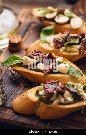 Sandwich mit Mozzarella-Käse, Pesto, sonnengetrockneten Tomaten, Basilikum und Thymian, serviert auf dem Holz Stockfoto