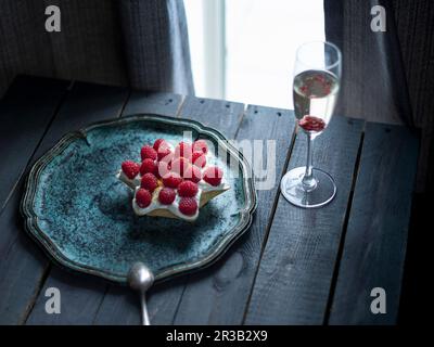 Ein sternförmiger Ricotta-Kuchen mit Himbeeren und einem Glas Champagner Stockfoto
