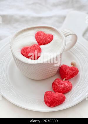 Eine Tasse weiße heiße Schokolade mit Schlagsahne und zwei rosa Herzmarshmallows Stockfoto