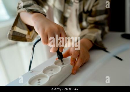 Junge, der das Kabel zu Hause in die Steckdose steckt Stockfoto