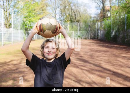 Lächelnder Junge, der Fußball auf dem Spielplatz hält Stockfoto