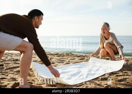 Glückliches Paar, das am Strand eine Decke auf Sand streut Stockfoto