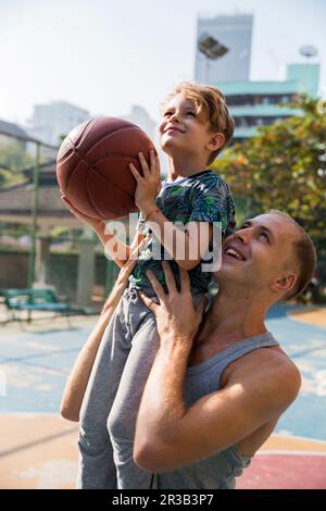 Glücklicher Vater mit Sohn, der an einem sonnigen Tag Basketball hält Stockfoto