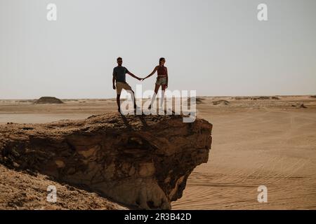 Ein Paar, das Händchen hält und auf einem Felsen in der Wüste steht Stockfoto