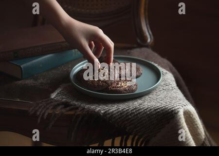 Schokoladenkekse auf dem Teller. Dark and Moody, Mystic Light Food-Fotografie. Kinderhände nehmen Stockfoto